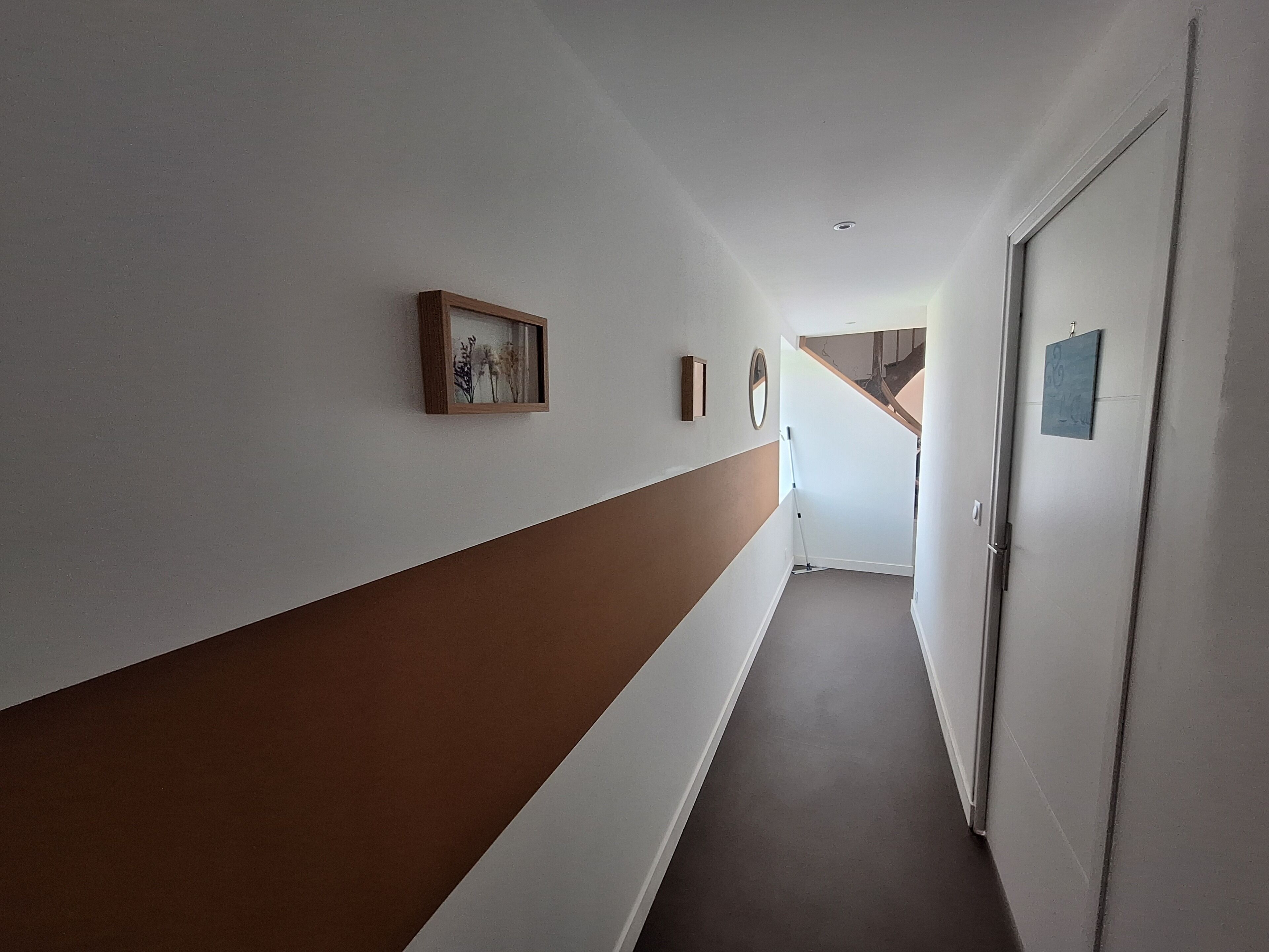 Un pasillo estrecho con pared marrón y blanca, una puerta a la derecha y una escalera al final.