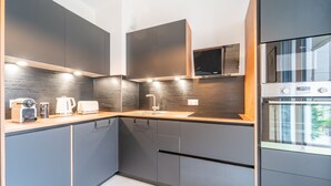 A modern kitchen with grey cabinets, a wooden countertop, a built-in microwave, and a stainless steel oven.