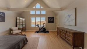 Un dormitorio amplio con un gran ventanal, un ventilador de techo, una cama, un aparador y una bicicleta estática.