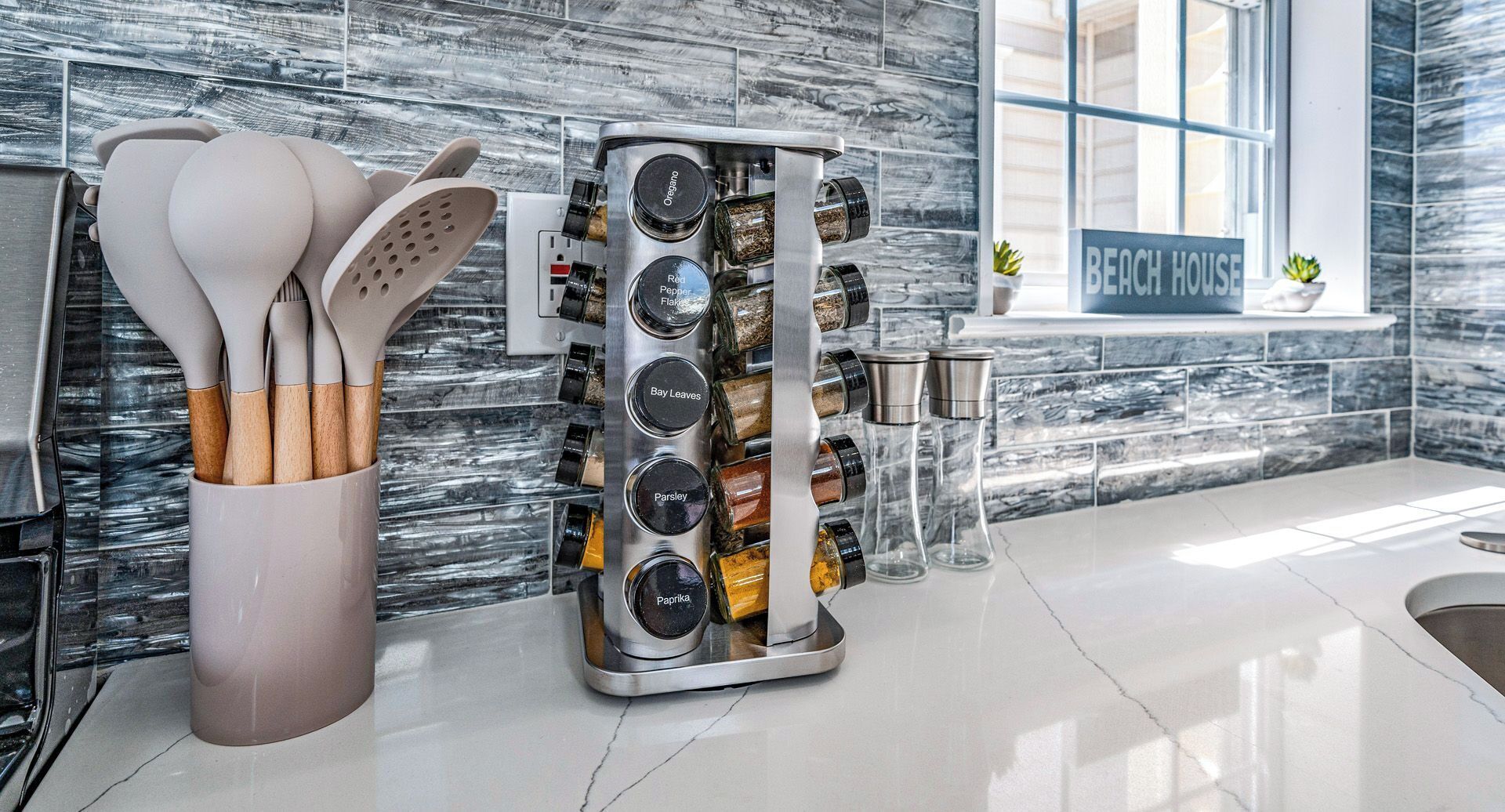 A kitchen with a spice rack, a utensil holder, and a 'BEACH HOUSE' sign.