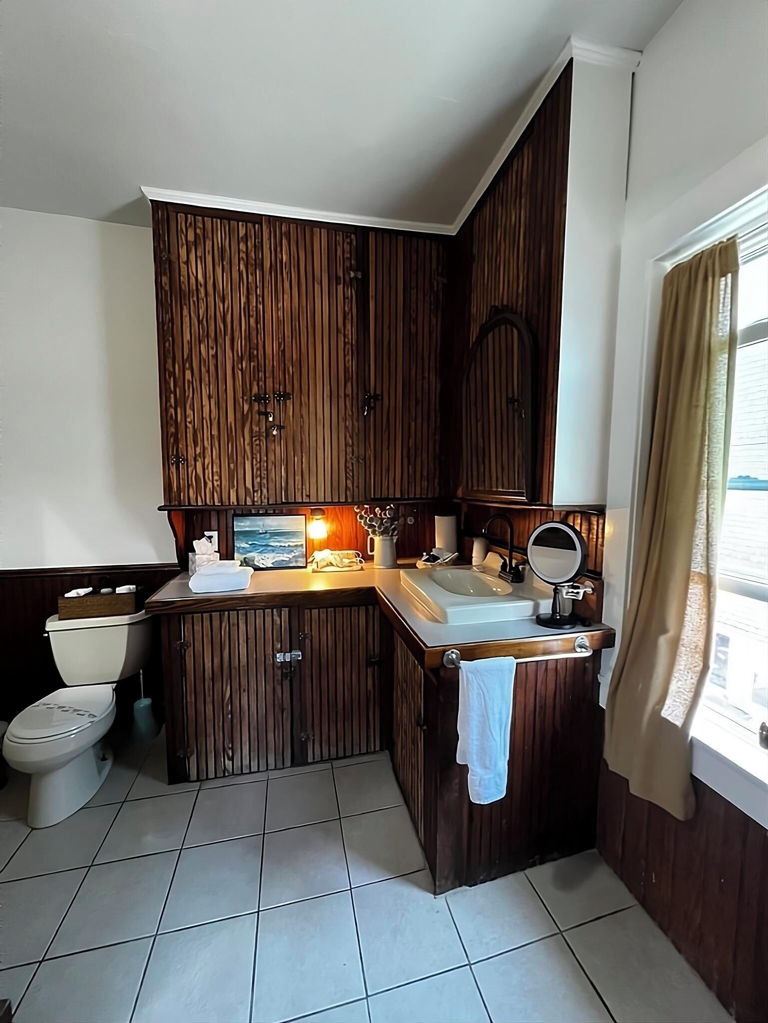 A compact bathroom with wooden cabinetry, a toilet, a sink, and a mirror.