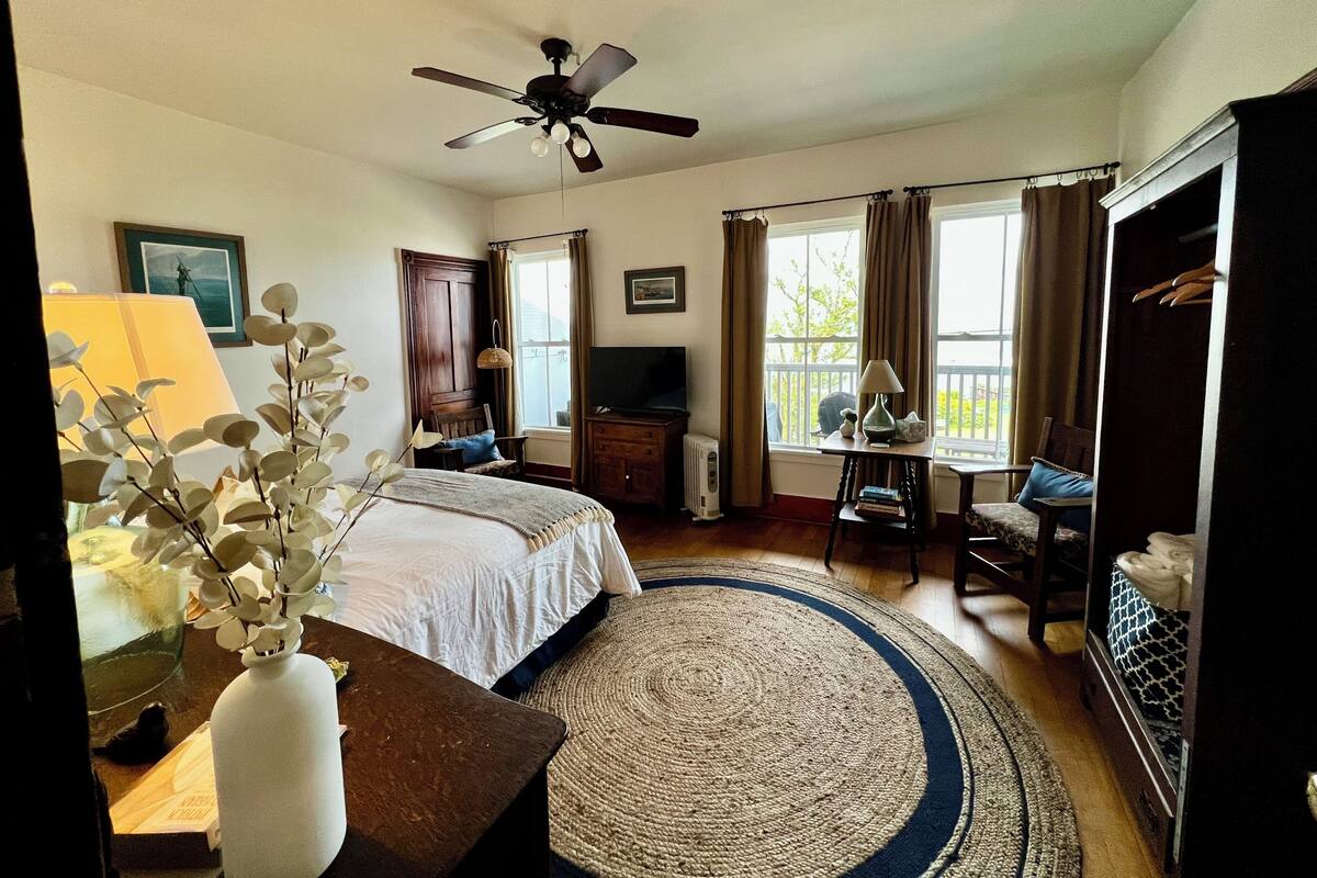 A hotel room with a bed, a desk, a TV, a ceiling fan, and a window with curtains.