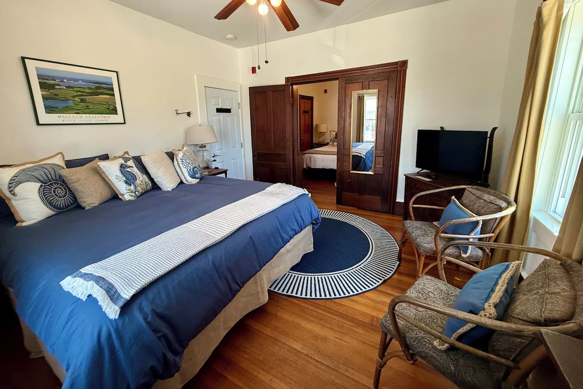 A bedroom with a large bed, a ceiling fan, a TV, and a wooden floor.