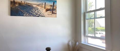 Una escalera con barandilla, un cuadro de una escena de playa y una ventana con vista a una casa y árboles.