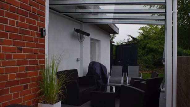 Un espace patio doté d’une véranda en verre, de mobilier d’extérieur et d’un mur en briques.