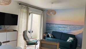 A bedroom with a bed, a chair, a sofa, a TV, and a mural of the ocean. - Belle Maison Avec Jardin et Parking Privée (Honfleur)