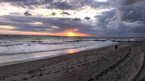 Une plage avec une jetée en bois qui s’avance dans l’eau, sous un ciel nuageux.