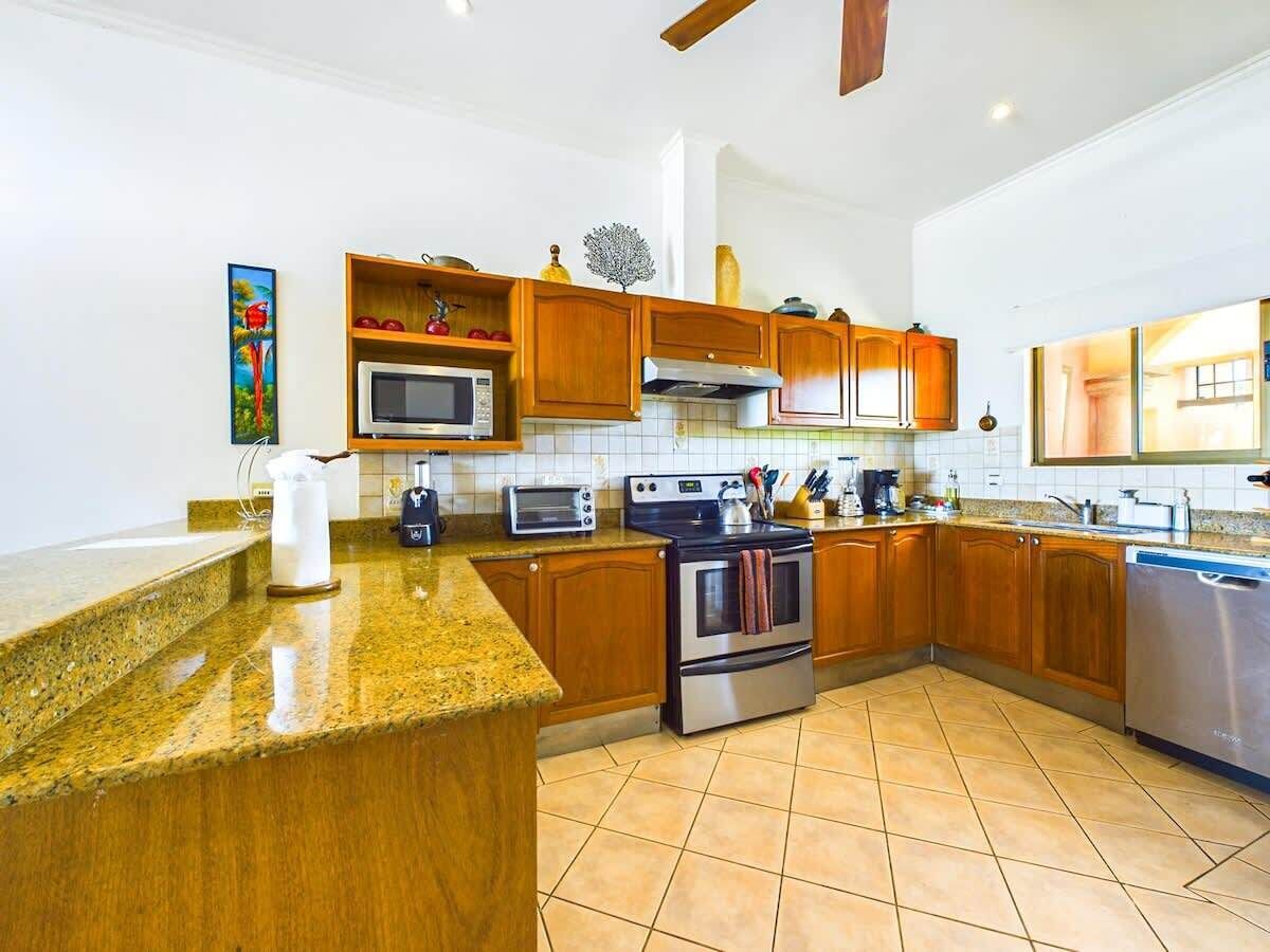 A modern kitchen with granite countertops, wooden cabinets, stainless steel appliances, and a tiled backsplash.