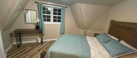 Un dormitorio con cama, escritorio y ventana con cortinas.