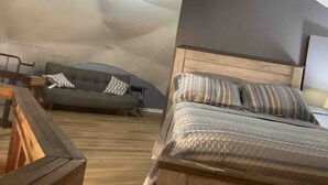 A cozy room with a bed, a sofa, and a wooden bench. - Domehouse DoverTN, near KY lake w event room, creek, pond & 4a fee hunting land. (Dover)