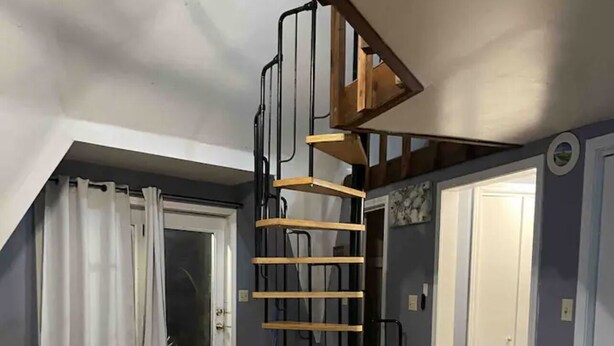A room with a sloped ceiling, wooden flooring, a spiral staircase, and a door leading to another room. - Domehouse DoverTN, near KY lake w event room, creek, pond & 4a fee hunting land. (Dover)
