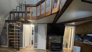 A loft-style room with a wooden staircase, a fireplace, and a kitchen area. - Domehouse DoverTN, near KY lake w event room, creek, pond & 4a fee hunting land. (Dover)