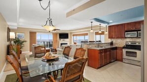 A spacious living area with a glass dining table, wooden chairs, a fireplace, and a view of the ocean. - 🏖️Serene Bayfront Bliss - Pristine 3 Bed/3Bath condo🏖️ (Ocean City)