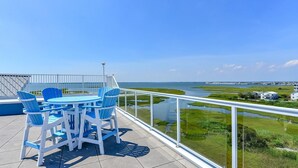 A balcony with a table and chairs, overlooking a coastal area with a water body and distant buildings. - 🏖️Serene Bayfront Bliss - Pristine 3 Bed/3Bath condo🏖️ (Ocean City)