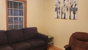 A living room with a dark brown sofa, a brown armchair, wooden flooring, a window with blinds, and a ceiling fan. - Cozy little home located in the Finger Lakes (Dundee)