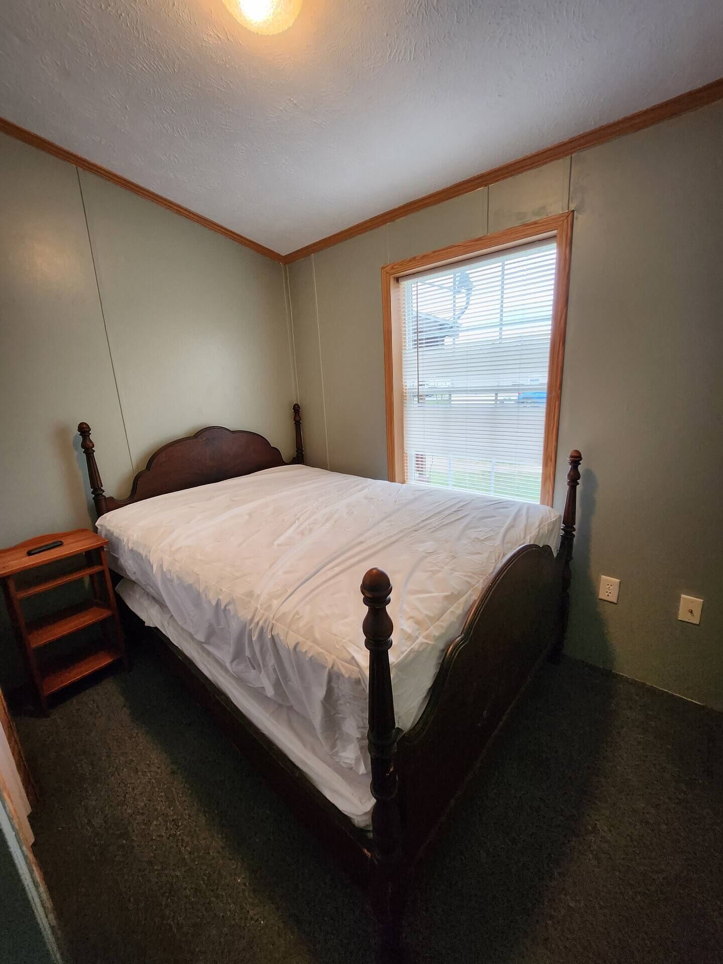 A bedroom with a single bed, a nightstand, a window with blinds, and a ceiling light.