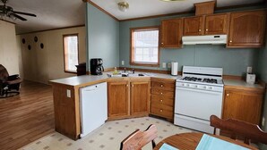 A compact kitchen with wooden cabinets, a white stove, and a dining area with a table and chairs. - Cozy little home located in the Finger Lakes (Dundee)