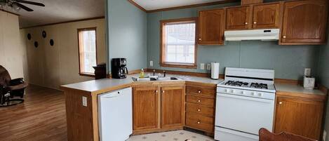 A compact kitchen with wooden cabinets, a white stove, and a dining area with a table and chairs.