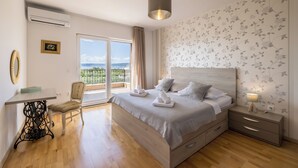Une chambre à coucher comprenant un lit, une table de chevet, une chaise, une table et donnant sur l’extérieur.
