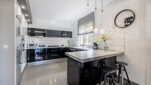 Une cuisine moderne dotée d’un îlot central, de tabourets de bar noirs et de luminaires suspendus.