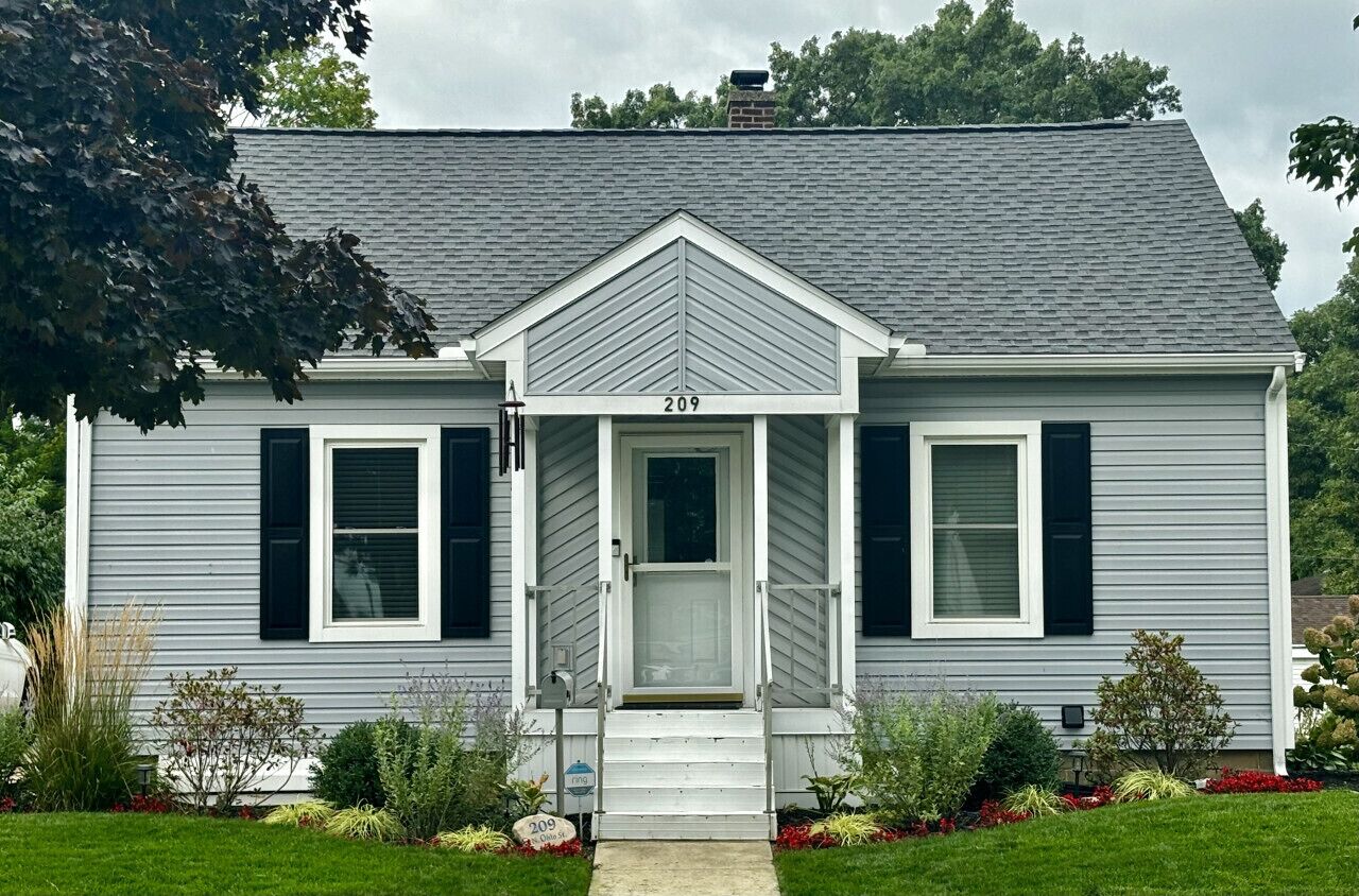 A single-story house with a gray exterior and black shutters, numbered 209.