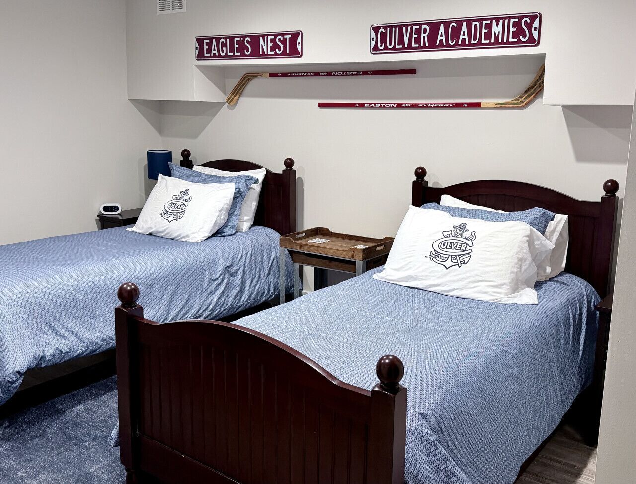 Two single beds with wooden headboards, a nightstand, and a wall-mounted shelf with hockey sticks and a sign.