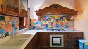 A kitchen with wooden cabinets, a tiled backsplash, a double sink, a stove, and a built-in oven. - Terrazza dei Coralli (Cefalù)