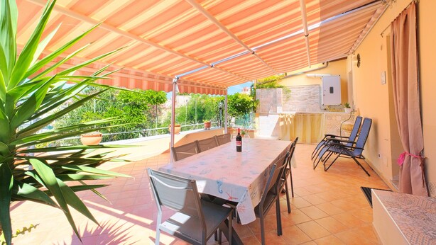 An outdoor patio with a table and chairs, a striped awning, and potted plants. - Terrazza dei Coralli (Cefalù)