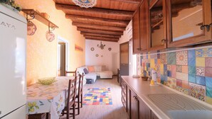 A kitchen with wooden cabinets, a refrigerator, a dining table with chairs, and a colorful tiled backsplash. - Terrazza dei Coralli (Cefalù)