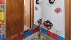 A bathroom with a round sink, colorful tiles, and decorative fish and octopus wall art. - Terrazza dei Coralli (Cefalù)