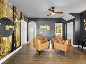 A modern living room with a round coffee table, leather armchairs, and a ceiling fan.