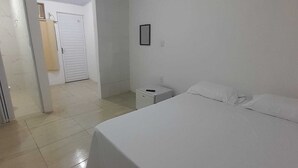 A clean, white room with a bed, a nightstand, and a door leading to another room. - Pousada Estelita Ponta de Areia Itaparic (Itaparica)