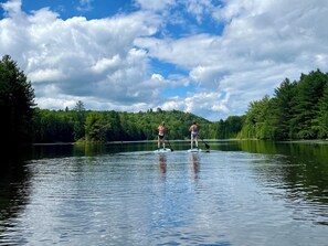 Two people paddleboarding on a calm lake surrounded by dense forest. - Luxury Cabin #3 Hot Tub, Kayaks, Paddle Boards, Private Fire Pit (Cavendish)
