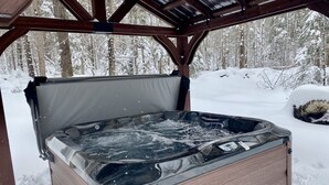 A hot tub in a wooden structure with a snowy forest background. - Cozy Chic! Cabin #3: wooded delights with year-round hot-tub and private firepit (Cavendish)