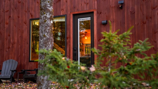 A wooden cabin with large windows, a door, and a small porch with Adirondack chairs. - Luxury Cabin #3 Hot Tub, Kayaks, Paddle Boards, Private Fire Pit (Cavendish)