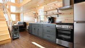 A modern kitchen with wooden walls, a stainless steel stove, and grey cabinets. - Cozy Chic! Cabin #3: wooded delights with year-round hot-tub and private firepit (Cavendish)