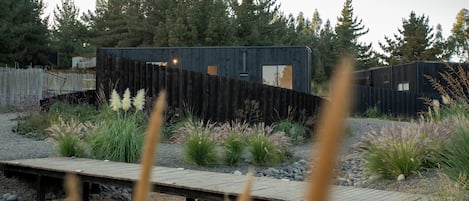 Une cabane moderne dotée d’une terrasse en bois, entourée d’un paysage naturel composé d’arbres et de plantes.