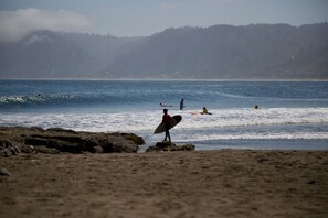 A beach with rocky terrain and a person holding a surfboard. - Bomar Lodge (Navidad)