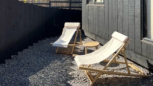 Un edificio moderno con dos ventanas, cerca de madera y dos sillones de relax sobre grava.
