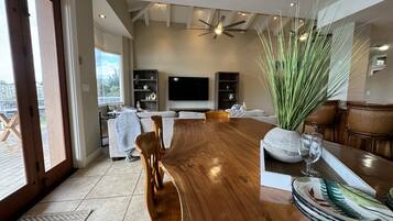A spacious living room with a wooden dining table, comfortable seating, a large window, and a ceiling fan.