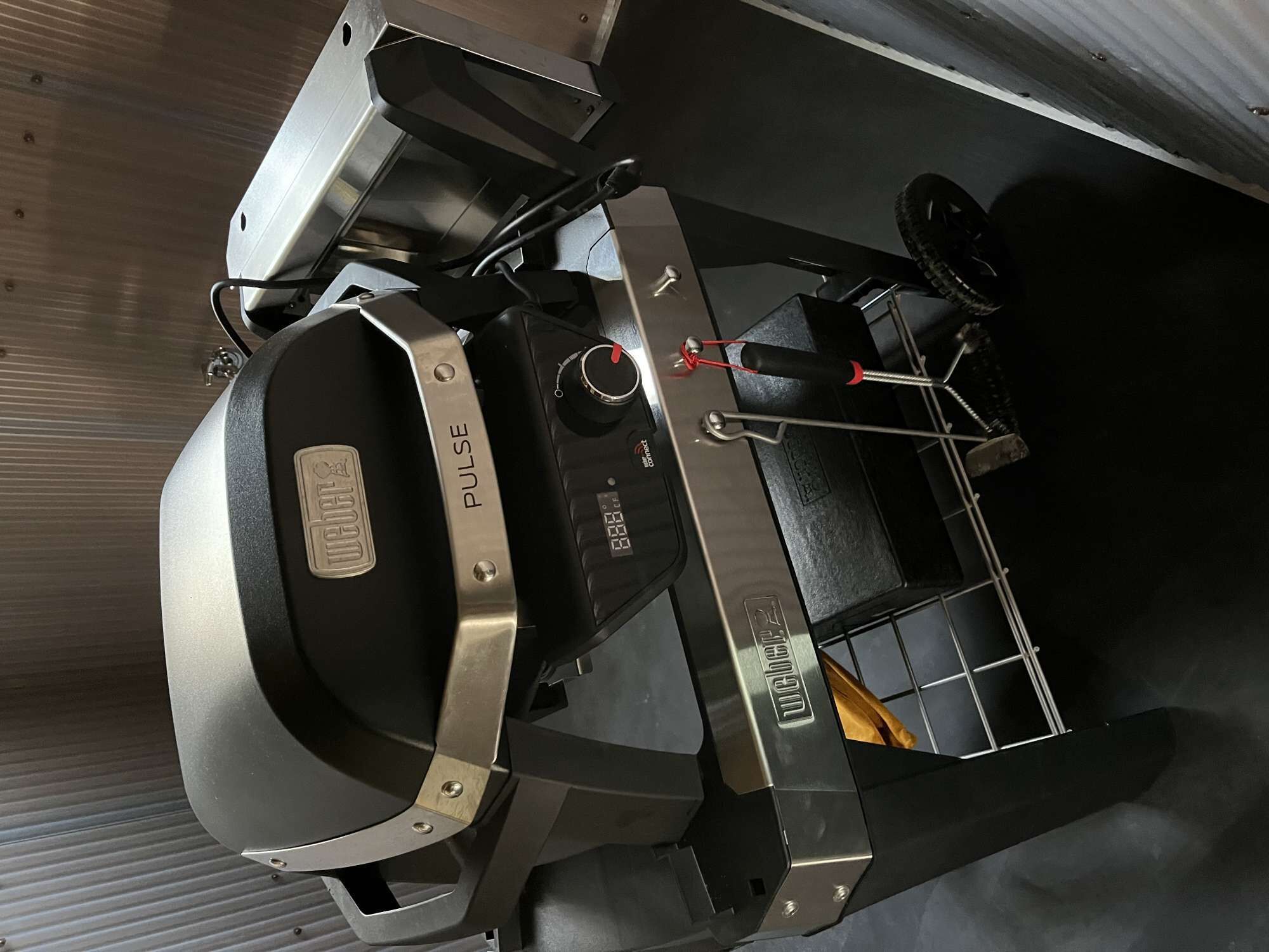 A kitchen with a microwave, a digital clock, and a metal rack.