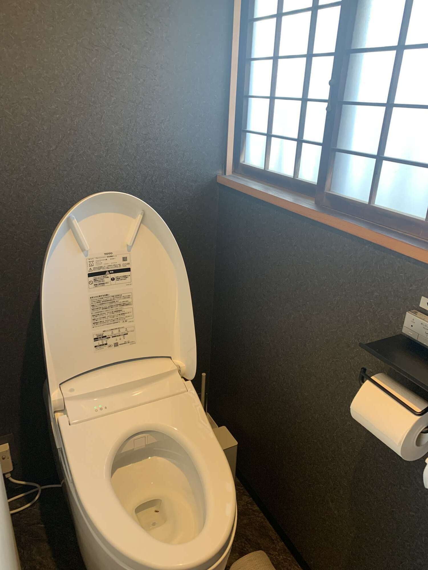Une petite salle de bain avec des toilettes, une fenêtre et une étagère sur laquelle se trouve un rouleau de papier toilette.