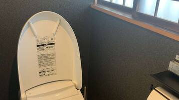 Une petite salle de bain avec des toilettes, une fenêtre et une étagère sur laquelle se trouve un rouleau de papier toilette.