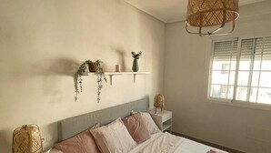 Ein ordentlich eingerichtetes Schlafzimmer mit Bett, Nachttischen, einer Hängelampe und einem Fenster mit Jalousien.