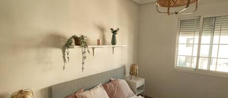 A neatly arranged bedroom with a bed, bedside tables, a hanging lamp, and a window with blinds.