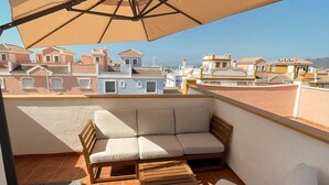 Ein Balkon mit beiger Markise, einer Holzsofa und einem Holzstuhl.