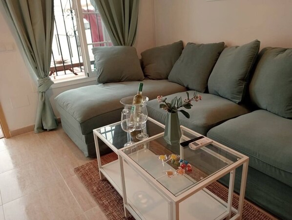 A living room with a glass coffee table, a sofa, and a window with curtains.