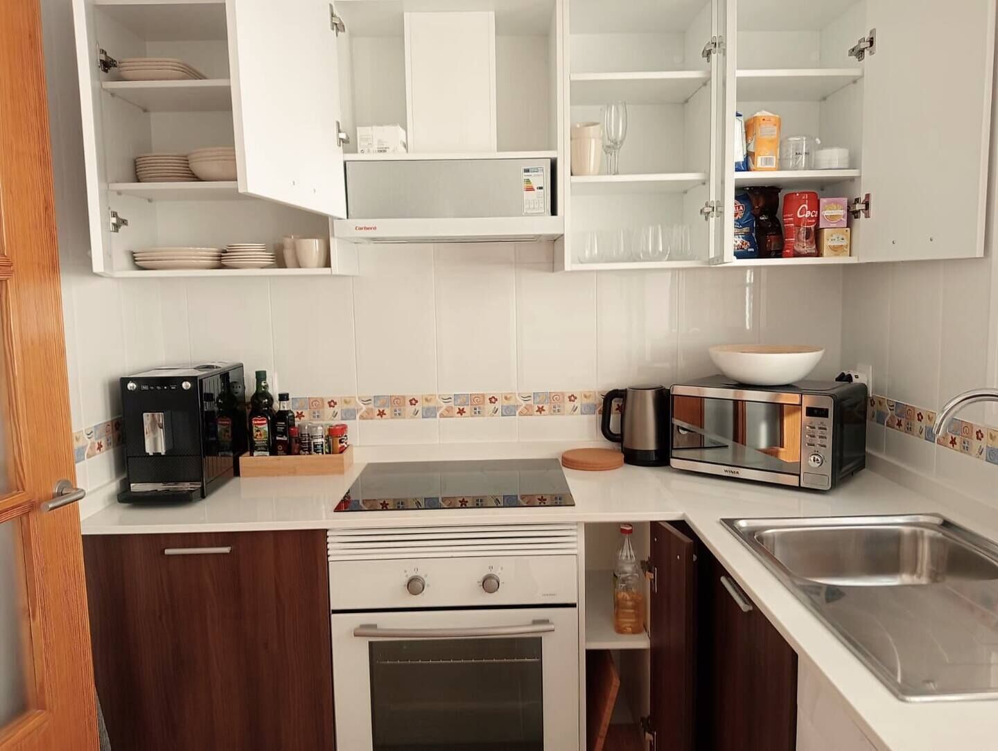 A kitchen with white cabinets, a stove, a microwave, a sink, and various kitchen appliances.