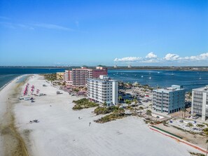 Un hotel frente a la playa con varias construcciones, una playa arenosa y barcos en el agua.