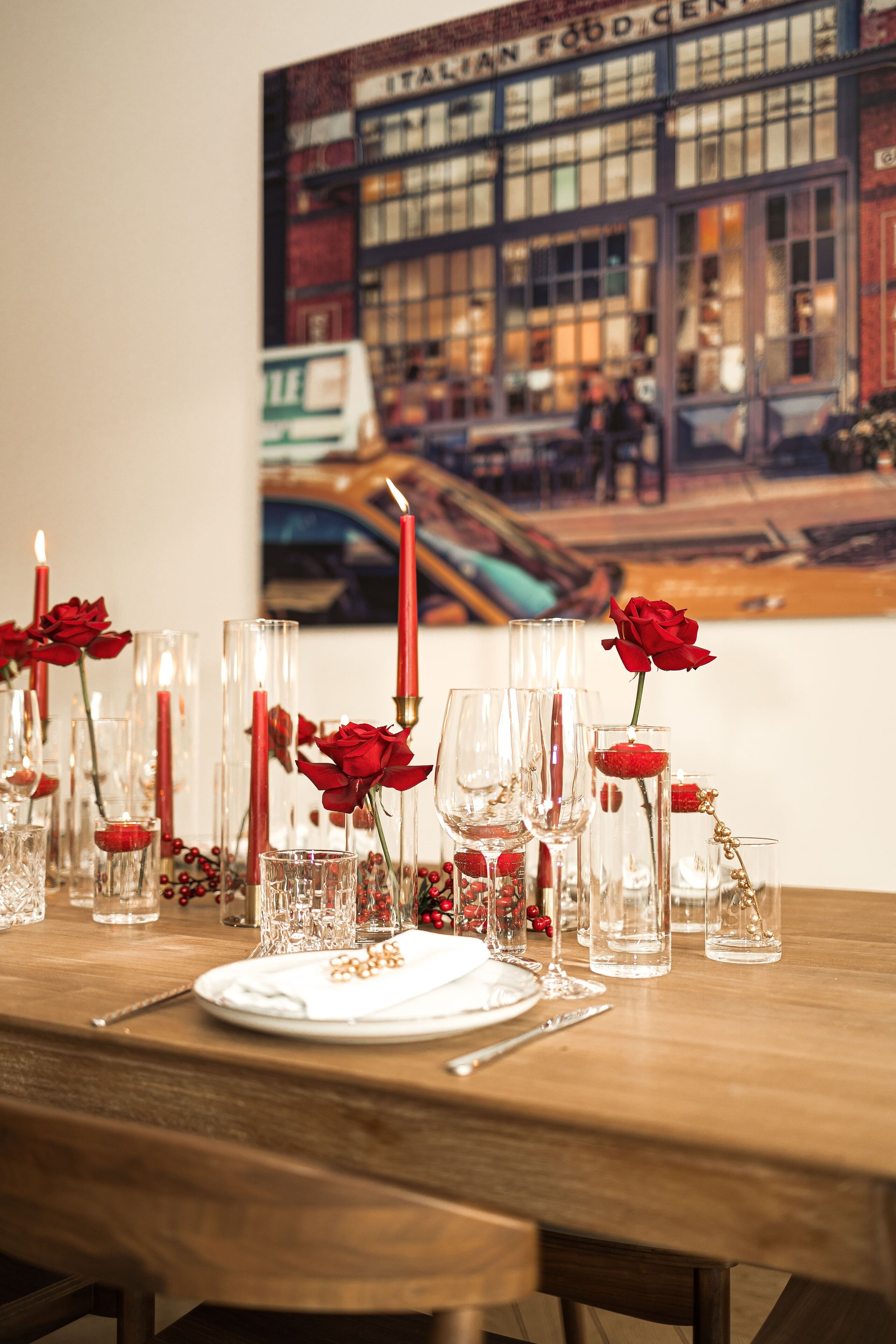 Een eettafel gedekt met helder glaswerk, rode rozen en kaarsen.